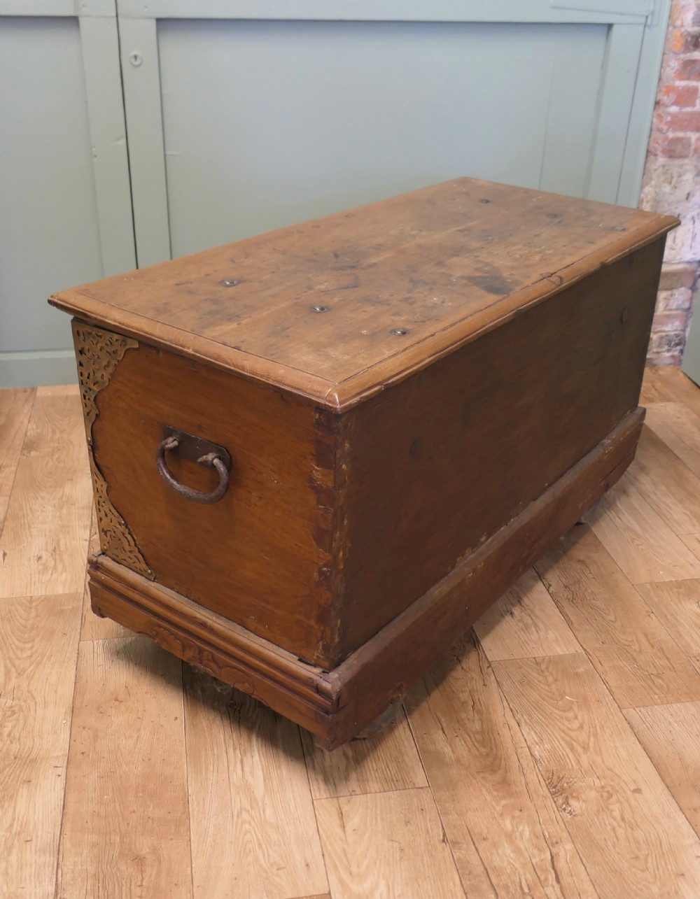 A rectangular carved elm wood storage coffer featuring decorative pierced brass corner mounts and a central lockplate above an ornate carved apron. View V