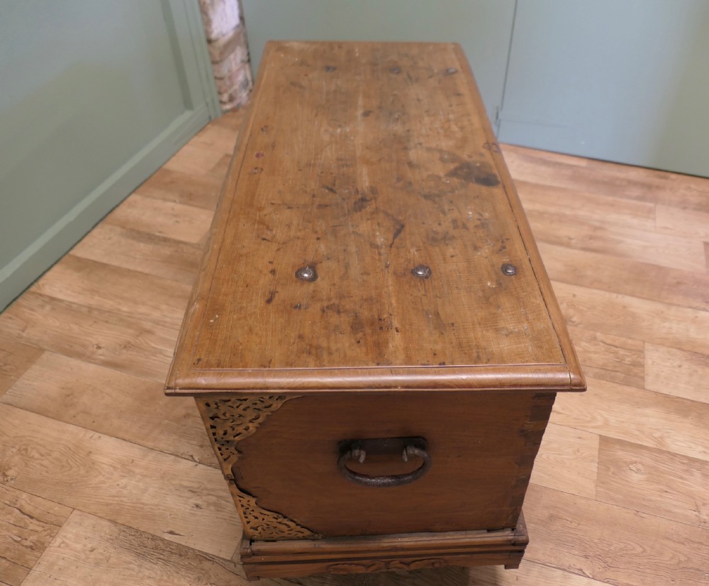 A rectangular carved elm wood storage coffer featuring decorative pierced brass corner mounts and a central lockplate above an ornate carved apron. View VI