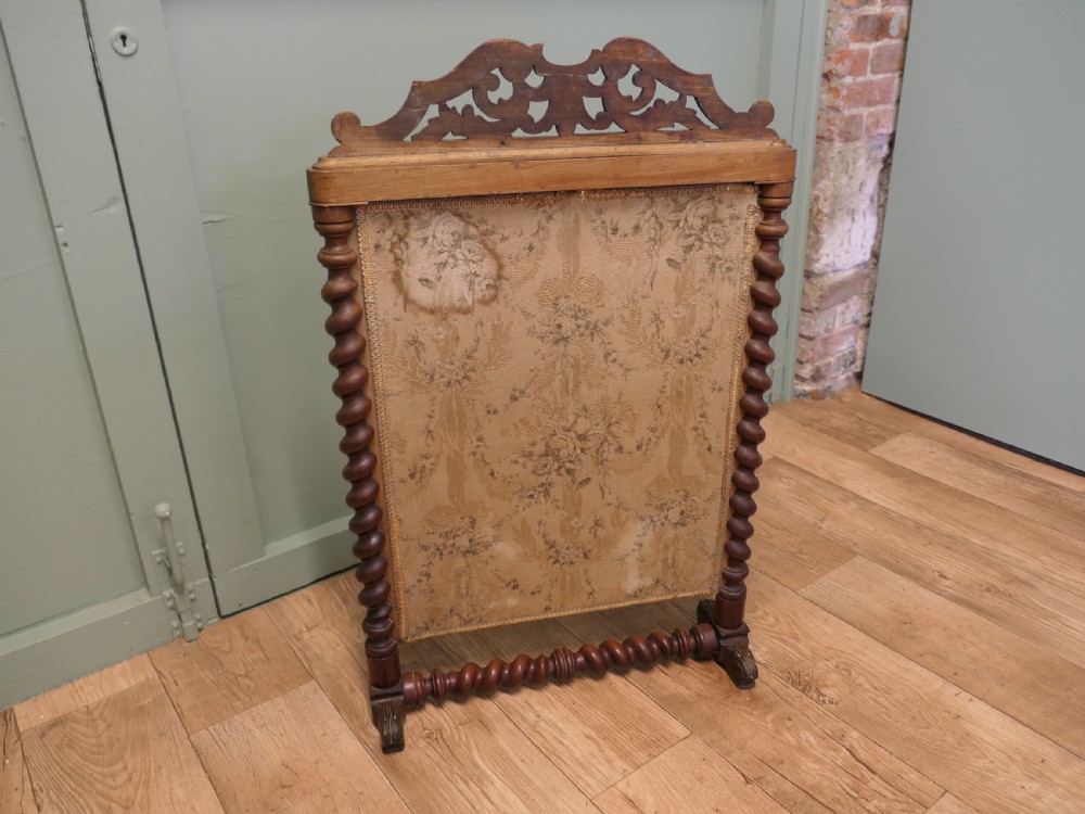 A Victorian mahogany fire screen featuring spiral barley twist supports, an openwork carved scroll cresting, and a central needlework panel depicting a colourful floral bouquet. View IV