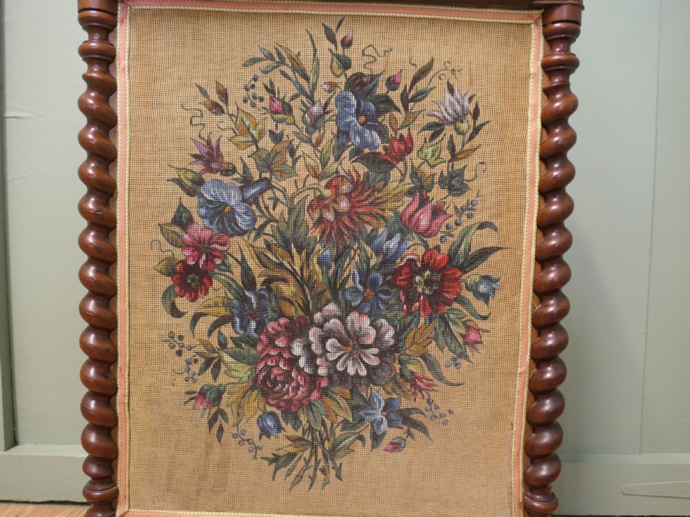 A Victorian mahogany fire screen featuring spiral barley twist supports, an openwork carved scroll cresting, and a central needlework panel depicting a colourful floral bouquet. View VI