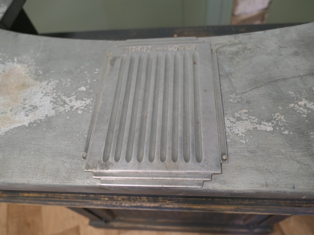 A distressed dark charcoal painted timber greeting desk with a zinc surface and an enamel plaque inscribed with the word Caisse. View III