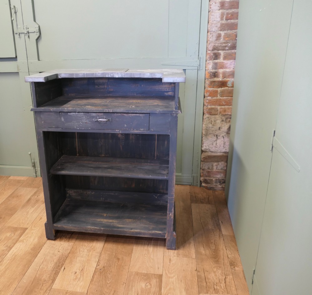 A distressed dark charcoal painted timber greeting desk with a zinc surface and an enamel plaque inscribed with the word Caisse. View VI