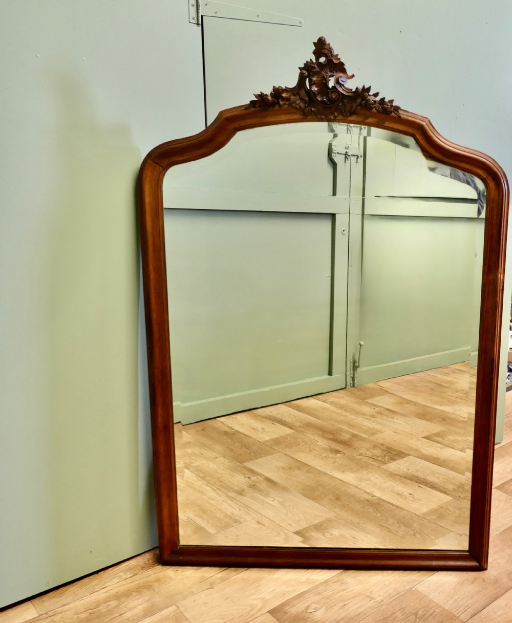 A tall wooden wall mirror featuring an arched frame topped with a carved cresting detail.