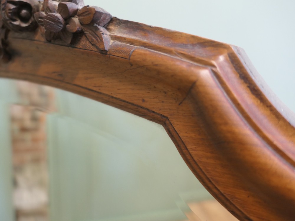 A tall wooden wall mirror featuring an arched frame topped with a carved cresting detail. View V