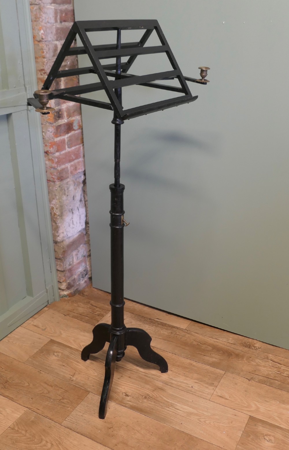 An ebonised wooden duet music stand featuring a double-sided slatted rest, height-adjustable central column, tripod base, and two brass candle sconces.