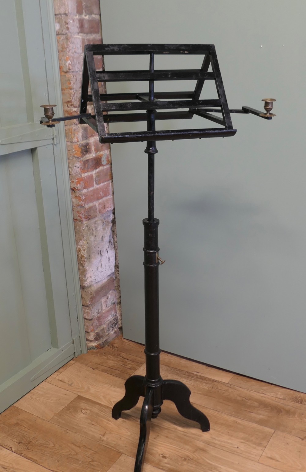 An ebonised wooden duet music stand featuring a double-sided slatted rest, height-adjustable central column, tripod base, and two brass candle sconces. View III
