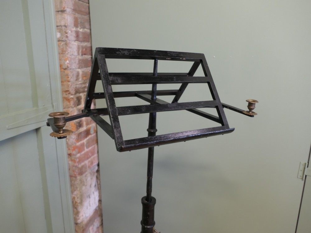 An ebonised wooden duet music stand featuring a double-sided slatted rest, height-adjustable central column, tripod base, and two brass candle sconces. View IV