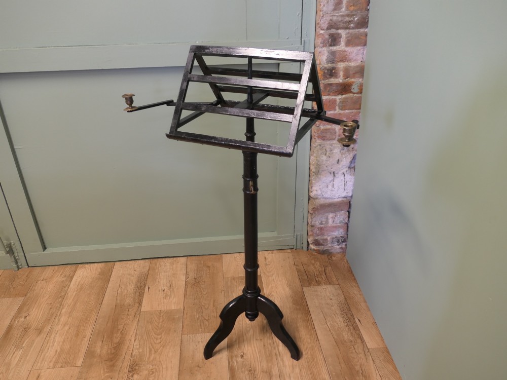 An ebonised wooden duet music stand featuring a double-sided slatted rest, height-adjustable central column, tripod base, and two brass candle sconces. View V