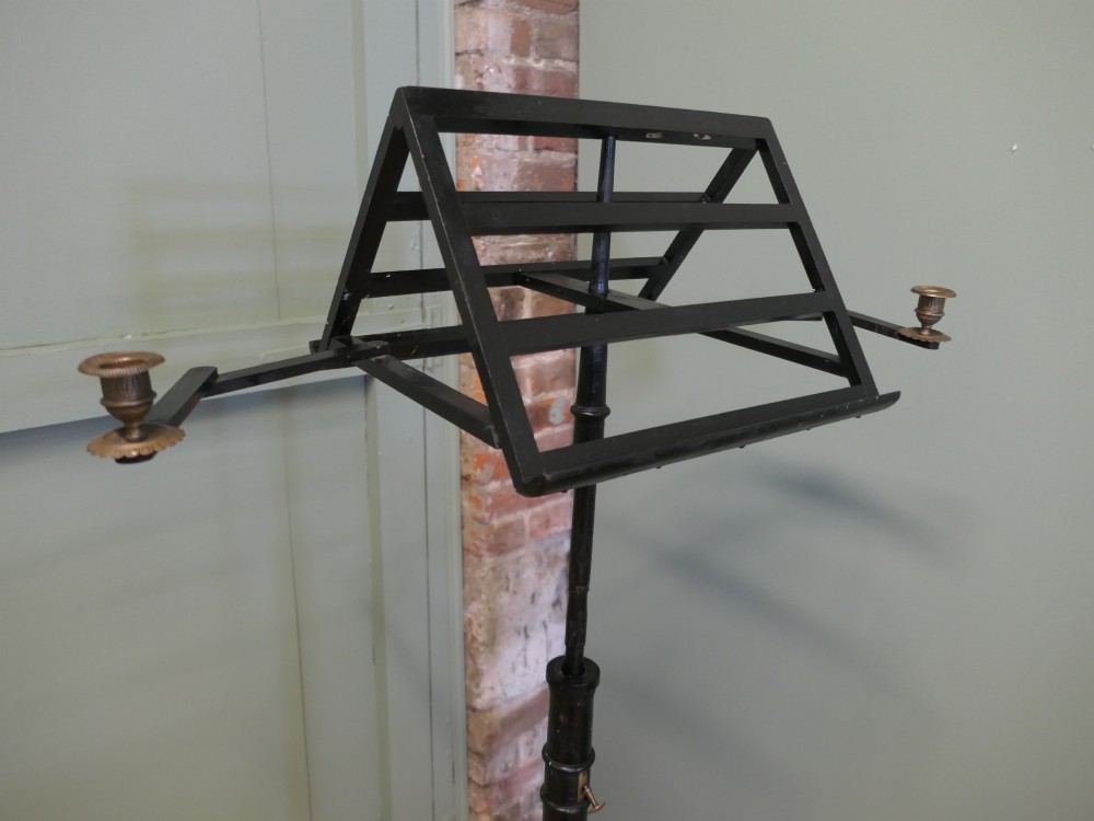 An ebonised wooden duet music stand featuring a double-sided slatted rest, height-adjustable central column, tripod base, and two brass candle sconces. View VI