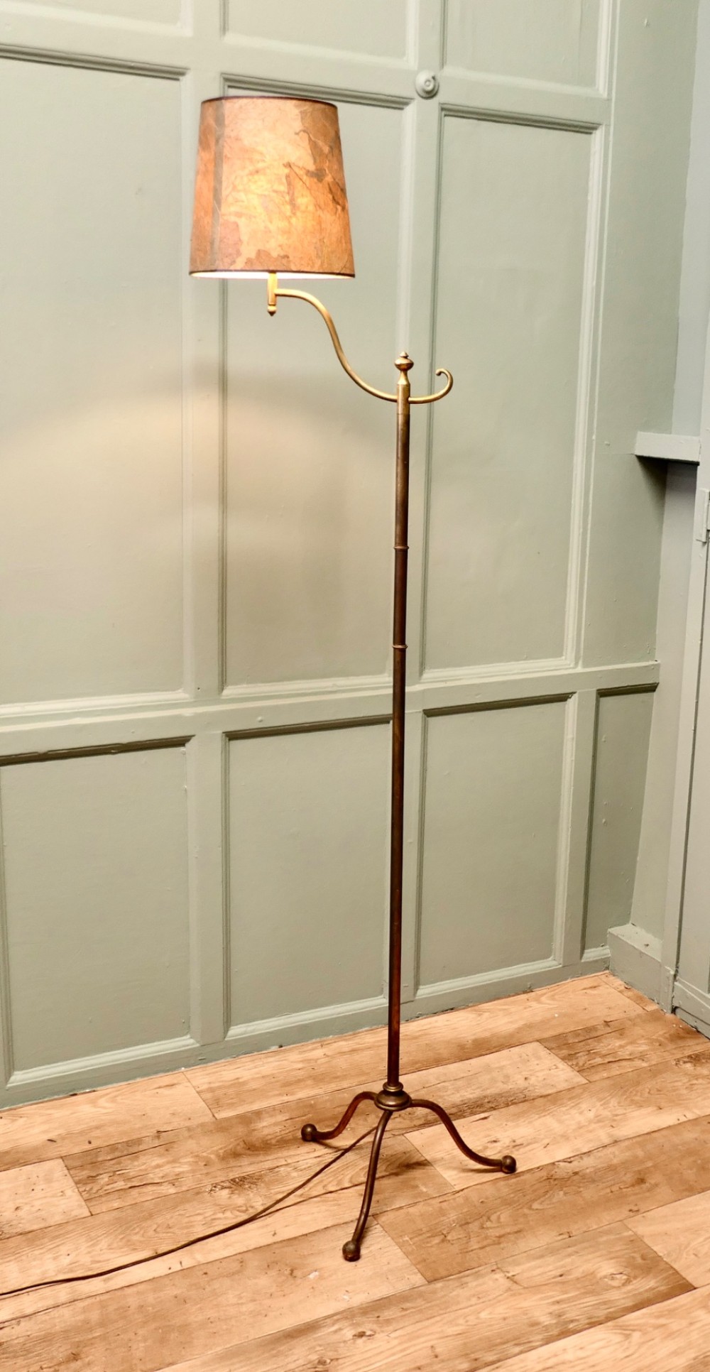 A French Arts and Crafts brass floor lamp featuring a slender stem, tripod base, curved adjustable arm, and a mottled parchment shade.