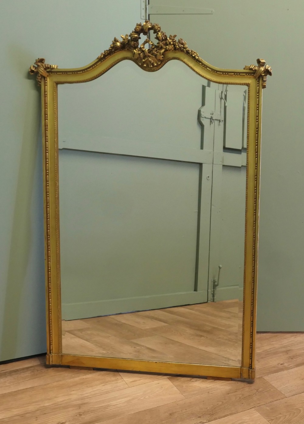 A large arched French Rococo mirror with a gold gilt frame featuring ribbon cresting, floral garlands, and bead moulding.