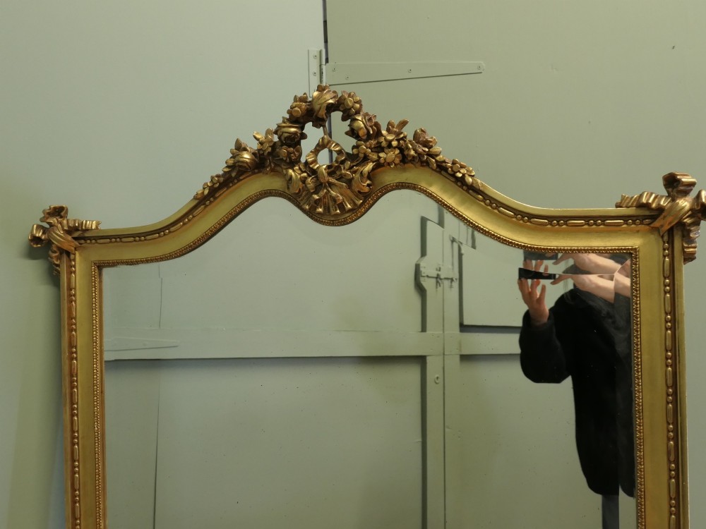 A large arched French Rococo mirror with a gold gilt frame featuring ribbon cresting, floral garlands, and bead moulding. View II
