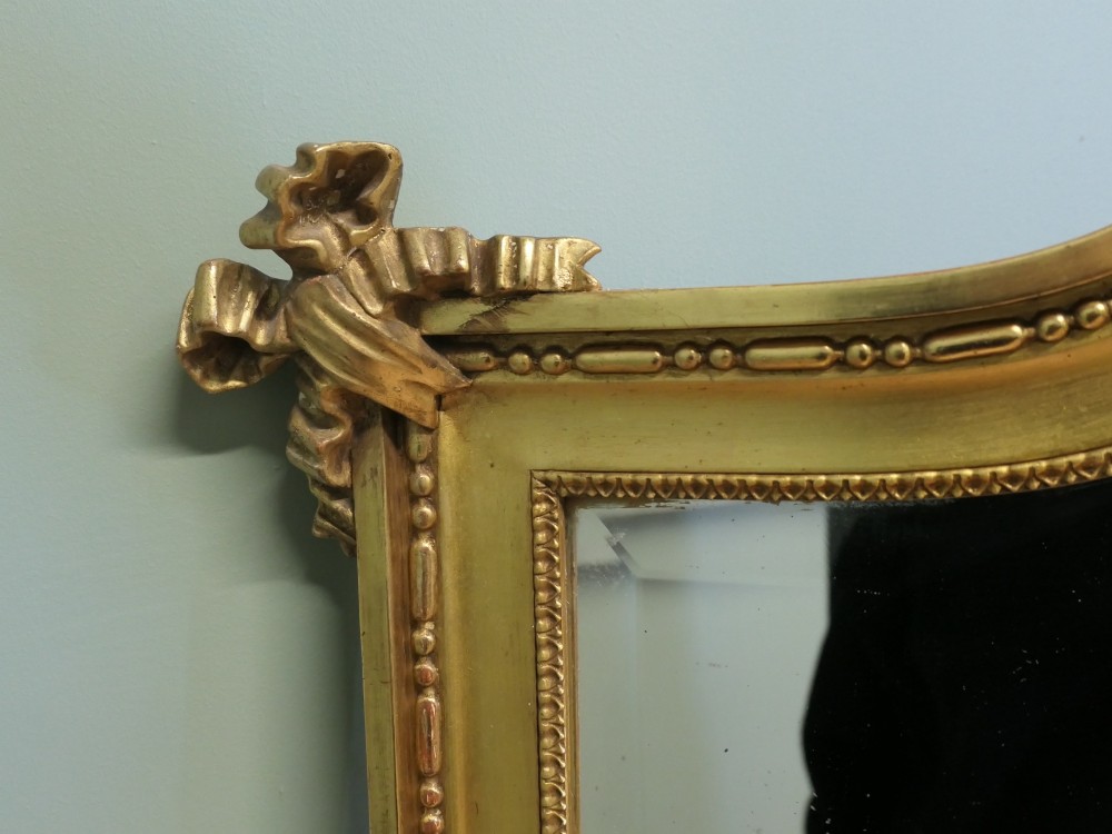 A large arched French Rococo mirror with a gold gilt frame featuring ribbon cresting, floral garlands, and bead moulding. View III