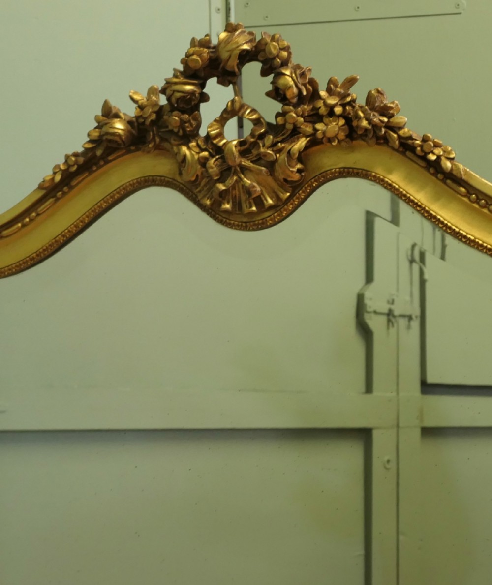 A large arched French Rococo mirror with a gold gilt frame featuring ribbon cresting, floral garlands, and bead moulding. View IV