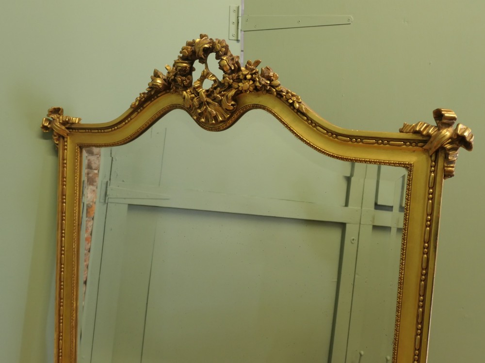 A large arched French Rococo mirror with a gold gilt frame featuring ribbon cresting, floral garlands, and bead moulding. View V