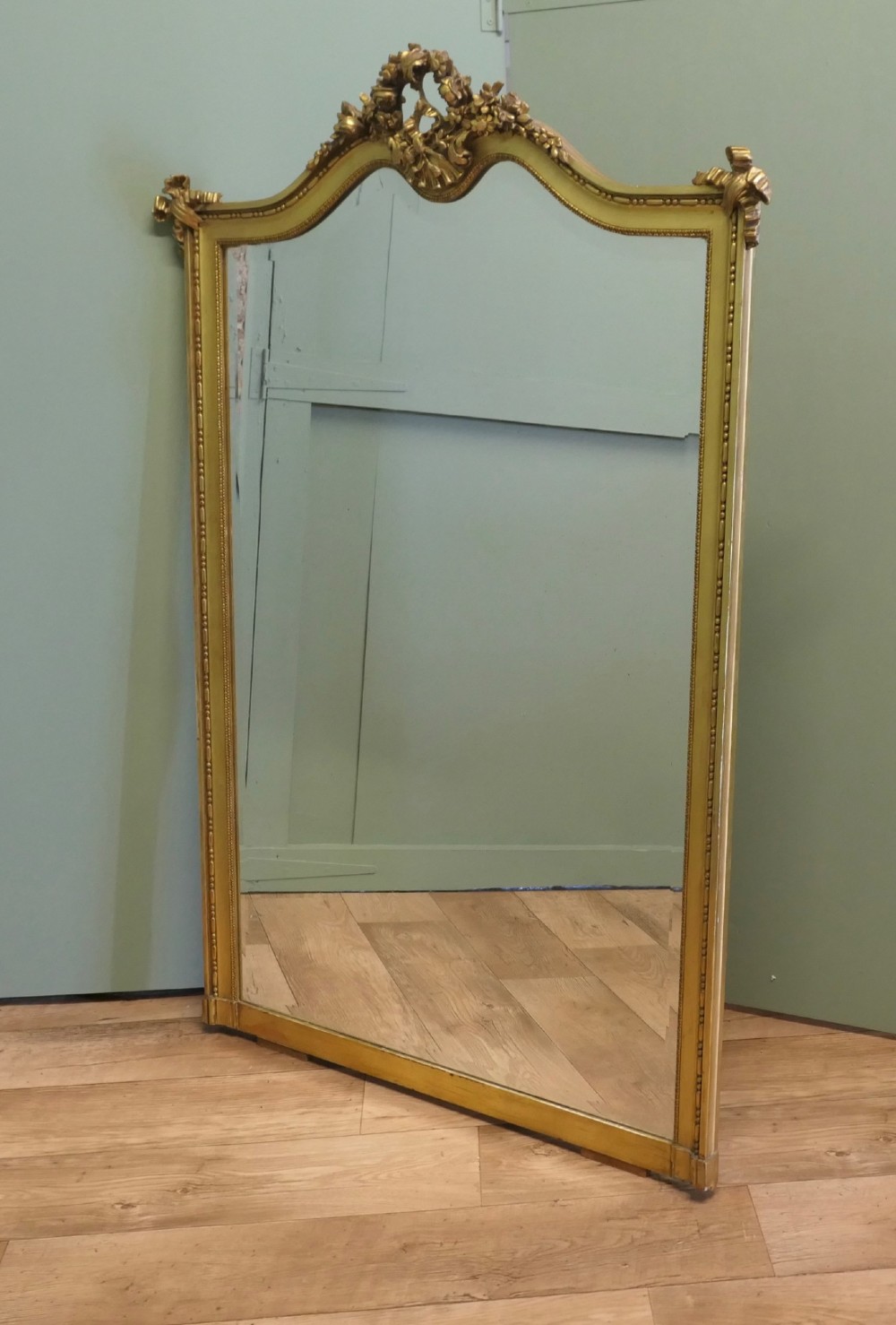 A large arched French Rococo mirror with a gold gilt frame featuring ribbon cresting, floral garlands, and bead moulding. View VI