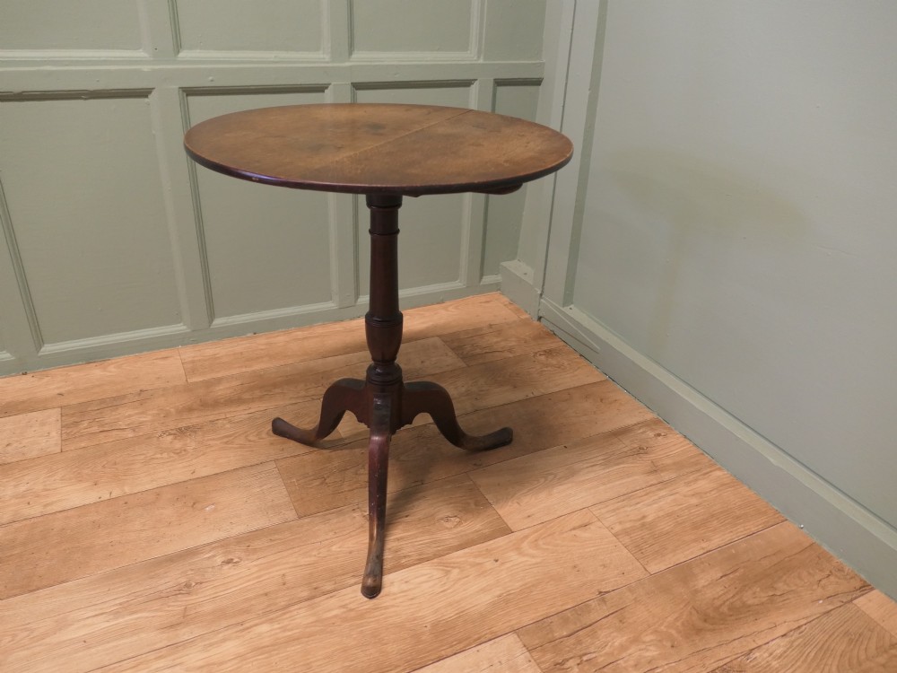 A circular solid oak tilt-top table with a turned central pedestal resting on three cabriole tripod feet.