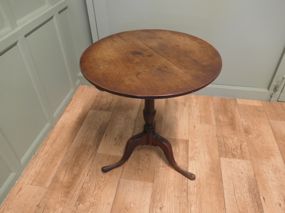 A circular solid oak tilt-top table with a turned central pedestal resting on three cabriole tripod feet. View III
