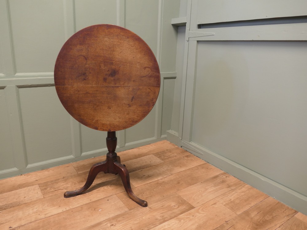 A circular solid oak tilt-top table with a turned central pedestal resting on three cabriole tripod feet. View V