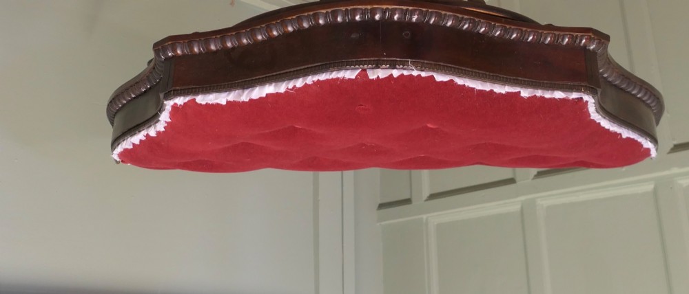 A 19th-century shaped wooden bed canopy corona featuring carved beaded moulding and a deep red button-tufted velvet underside with white ruffled trim. View II