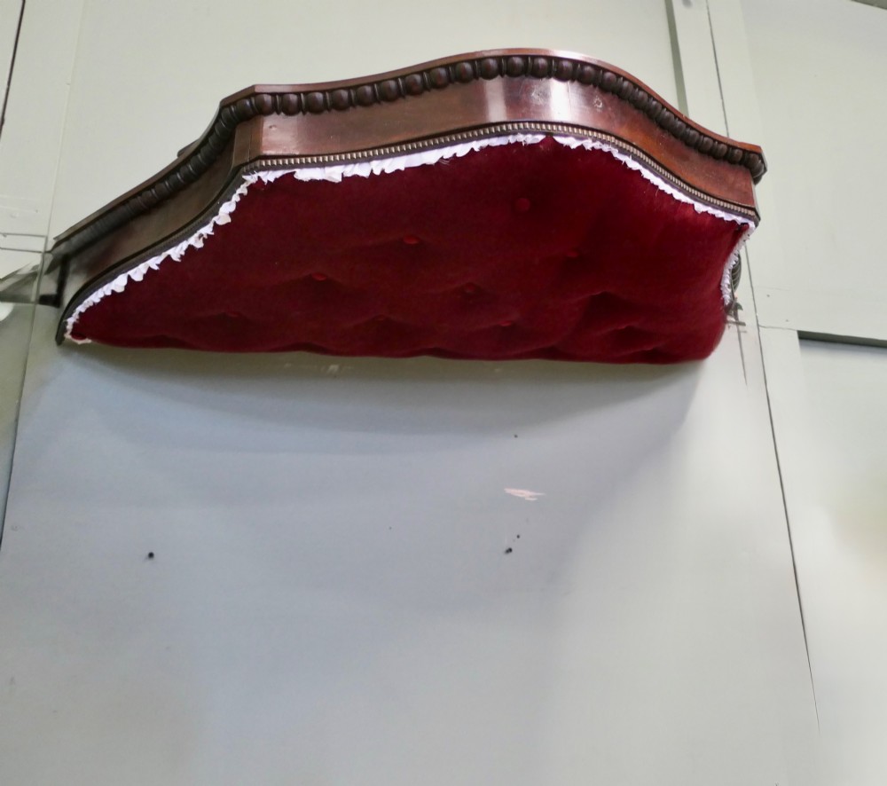 A 19th-century shaped wooden bed canopy corona featuring carved beaded moulding and a deep red button-tufted velvet underside with white ruffled trim. View IV
