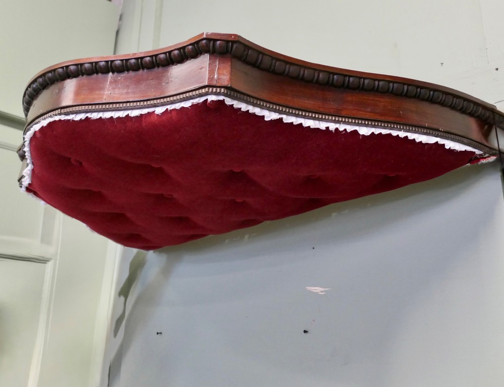 A 19th-century shaped wooden bed canopy corona featuring carved beaded moulding and a deep red button-tufted velvet underside with white ruffled trim. View V