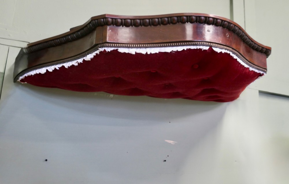 A 19th-century shaped wooden bed canopy corona featuring carved beaded moulding and a deep red button-tufted velvet underside with white ruffled trim. View VI