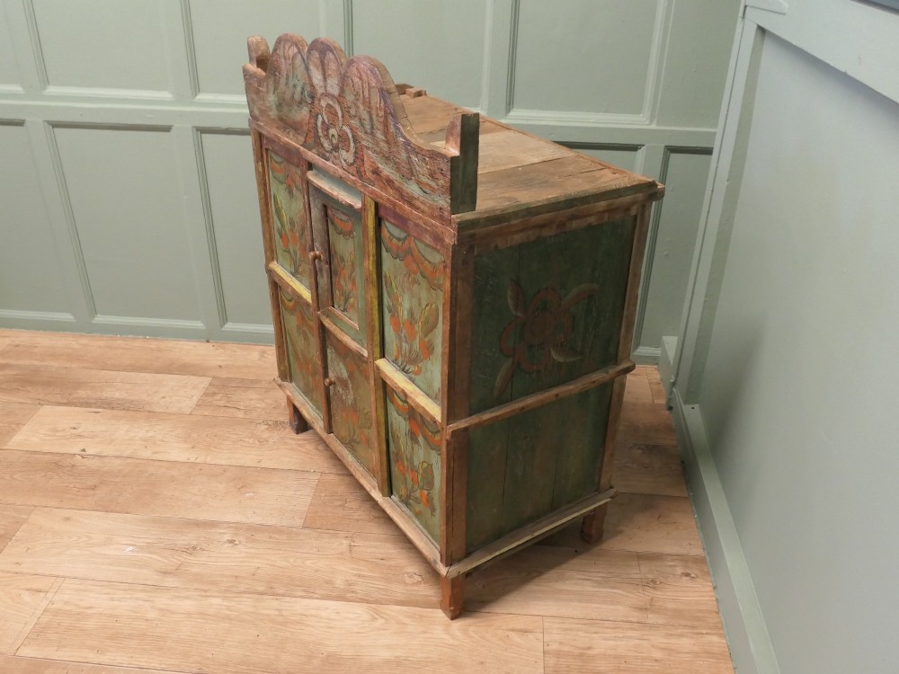A rustic French folk art painted pine cupboard with green and orange floral panels and a scalloped gallery top. View II