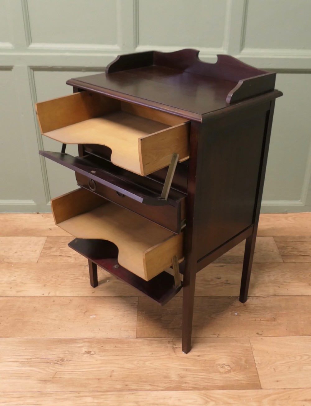 An Edwardian dark mahogany music cabinet with a raised shaped gallery back, standing on four straight legs with four drop-front drawers open to show internal slides. View IV