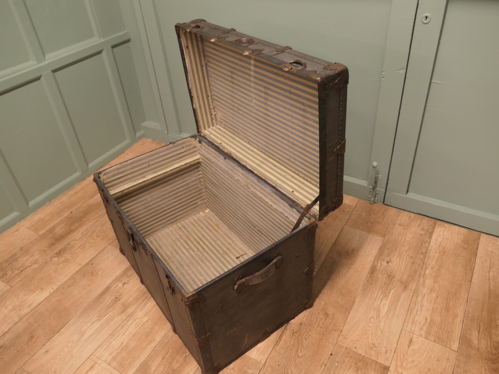 A rectangular dark grey vintage travel trunk with studded edges, metal corner protectors, and brass latch locks. View III