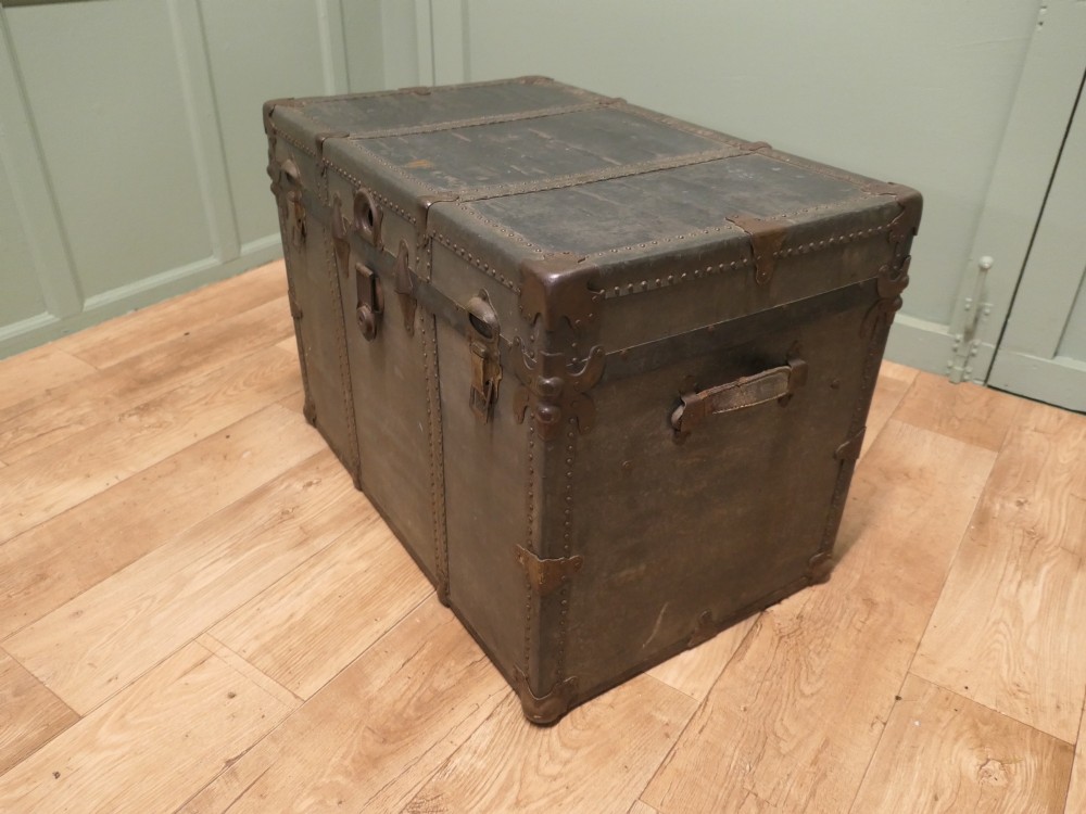 A rectangular dark grey vintage travel trunk with studded edges, metal corner protectors, and brass latch locks. View V