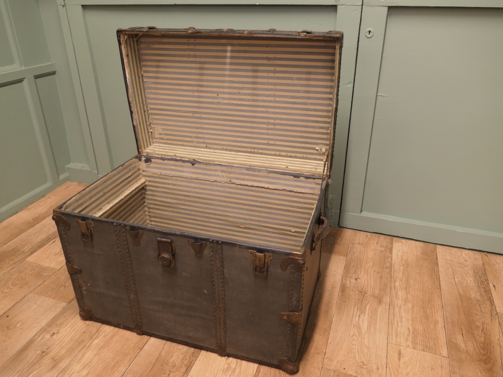 A rectangular dark grey vintage travel trunk with studded edges, metal corner protectors, and brass latch locks. View VII