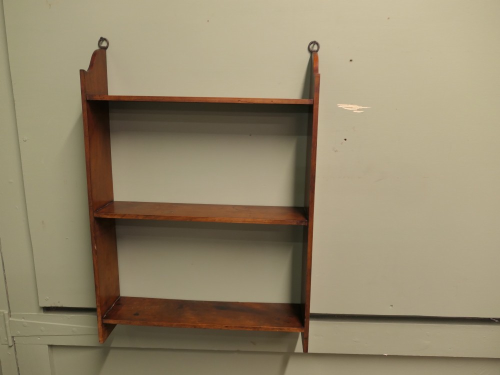 A three-tier open wooden wall shelf unit with a warm brown finish and metal hanging rings at the top.