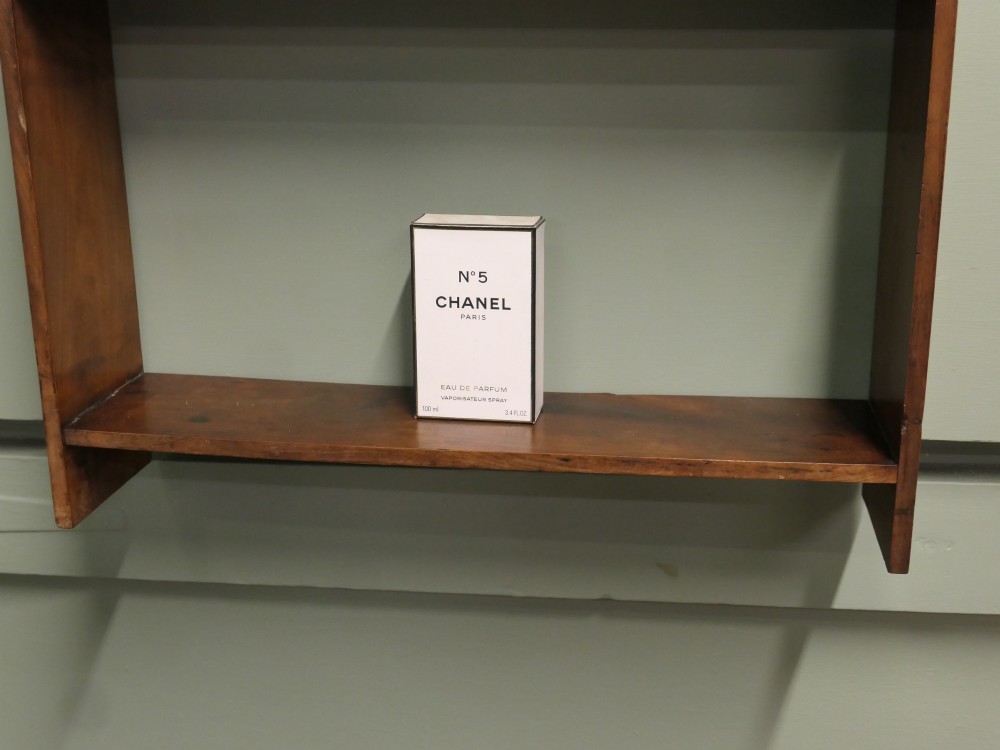 A three-tier open wooden wall shelf unit with a warm brown finish and metal hanging rings at the top. View IV