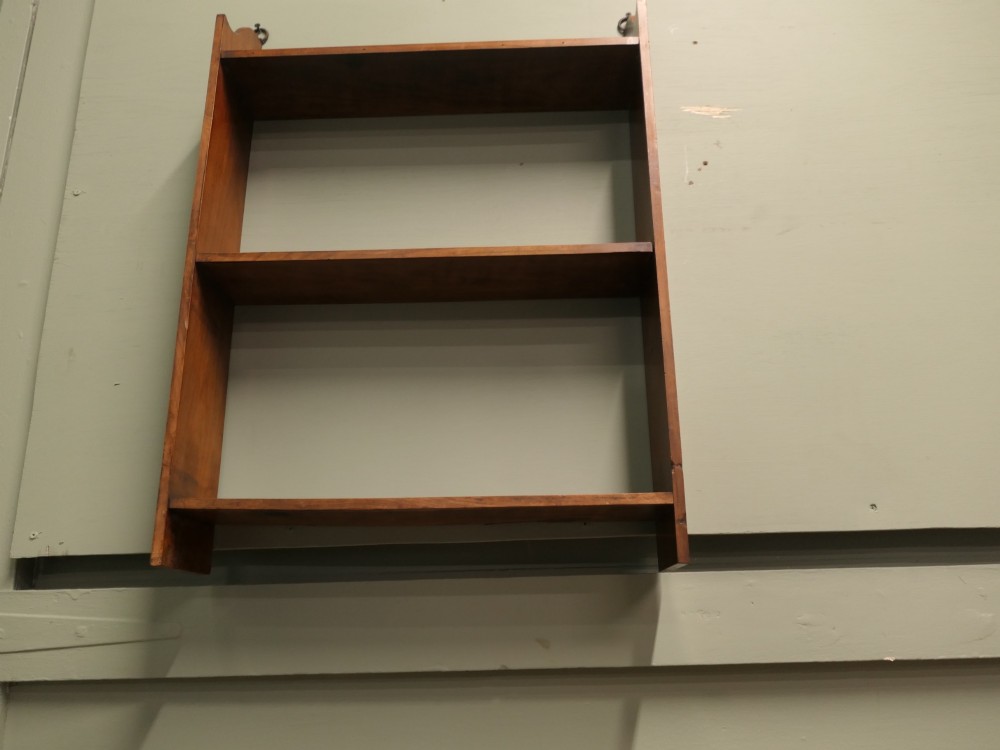 A three-tier open wooden wall shelf unit with a warm brown finish and metal hanging rings at the top. View V
