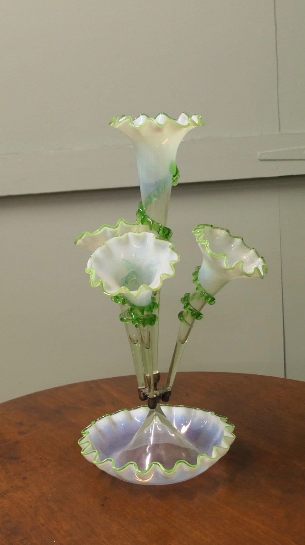 A nineteenth-century hand-blown uranium glass epergne featuring four crimped trumpet stems with applied green glass trailing mounted above an opalescent bowl base.