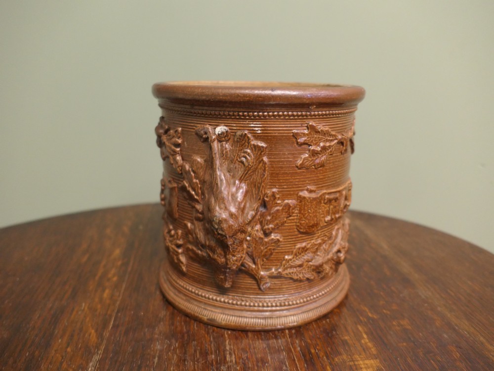 A cylindrical brown glazed stoneware tobacco pot featuring raised lettering that reads TABAC surrounded by oak leaf and acorn garlands. View II