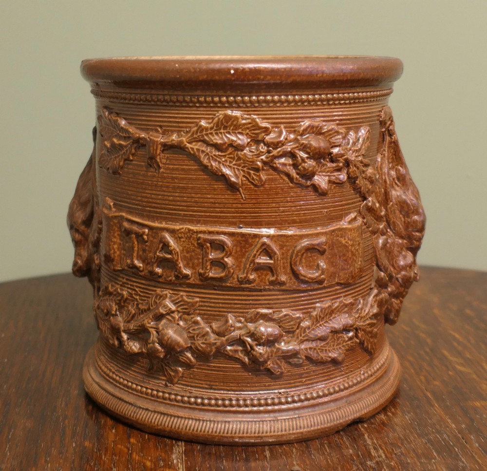 A cylindrical brown glazed stoneware tobacco pot featuring raised lettering that reads TABAC surrounded by oak leaf and acorn garlands. View IV