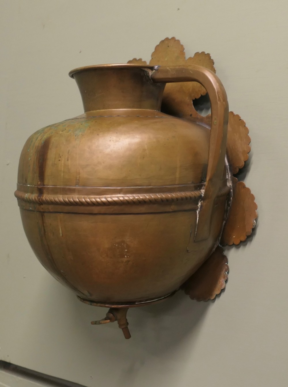 A hand-crafted copper and brass wall-mounted water reservoir featuring a scalloped backplate, rope-twist waist band, and lower tap.