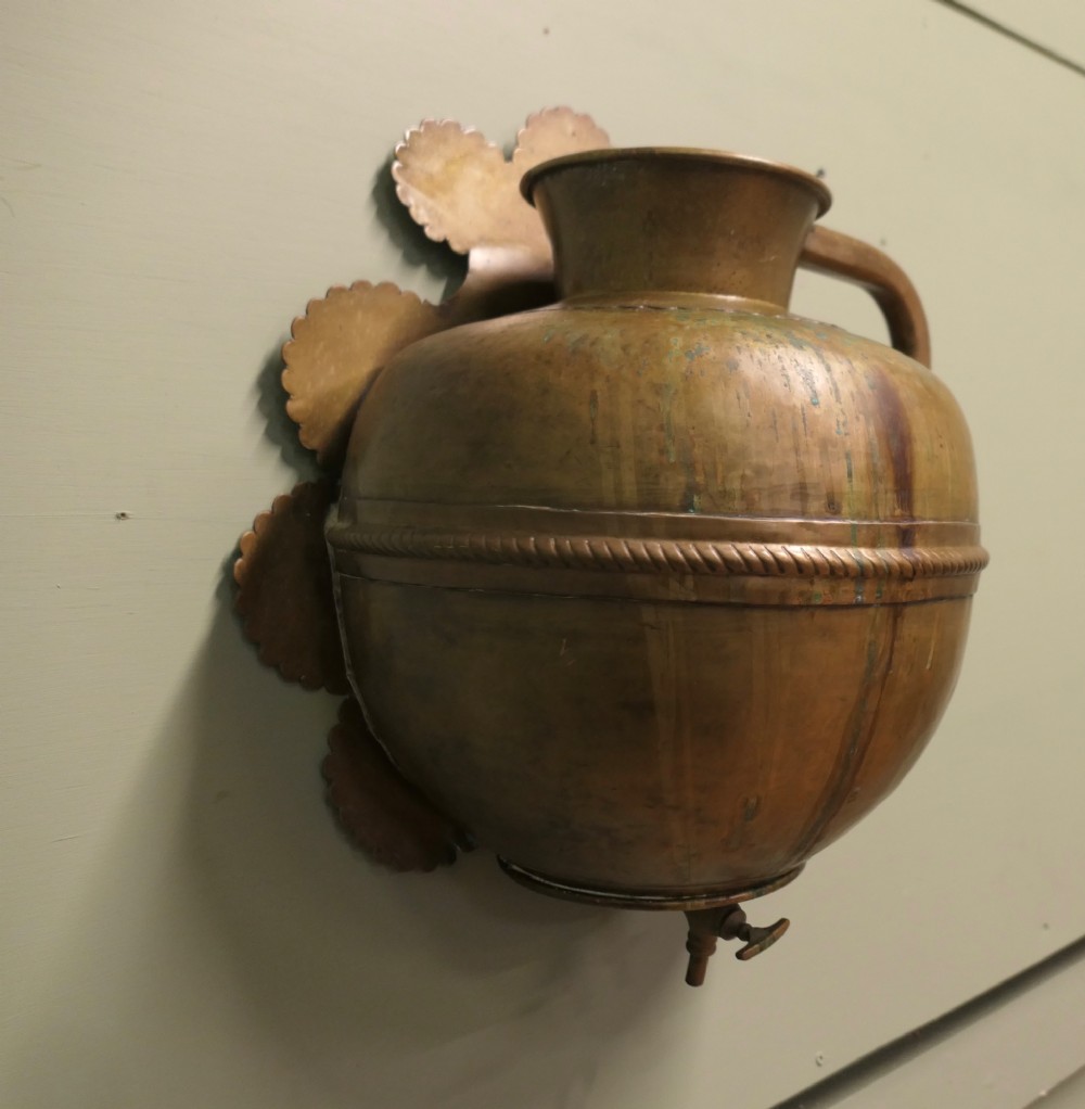 A hand-crafted copper and brass wall-mounted water reservoir featuring a scalloped backplate, rope-twist waist band, and lower tap. View II