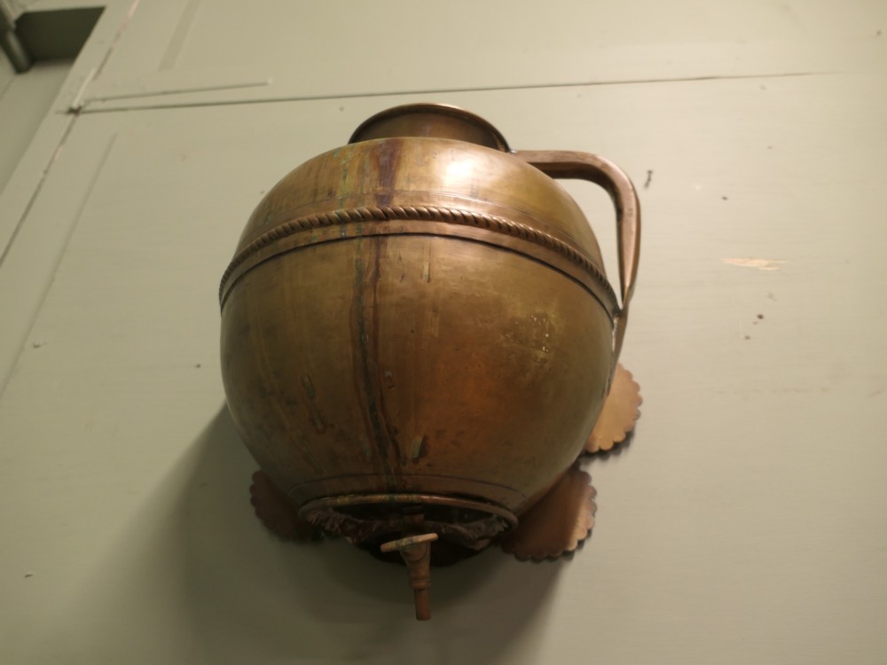 A hand-crafted copper and brass wall-mounted water reservoir featuring a scalloped backplate, rope-twist waist band, and lower tap. View VII