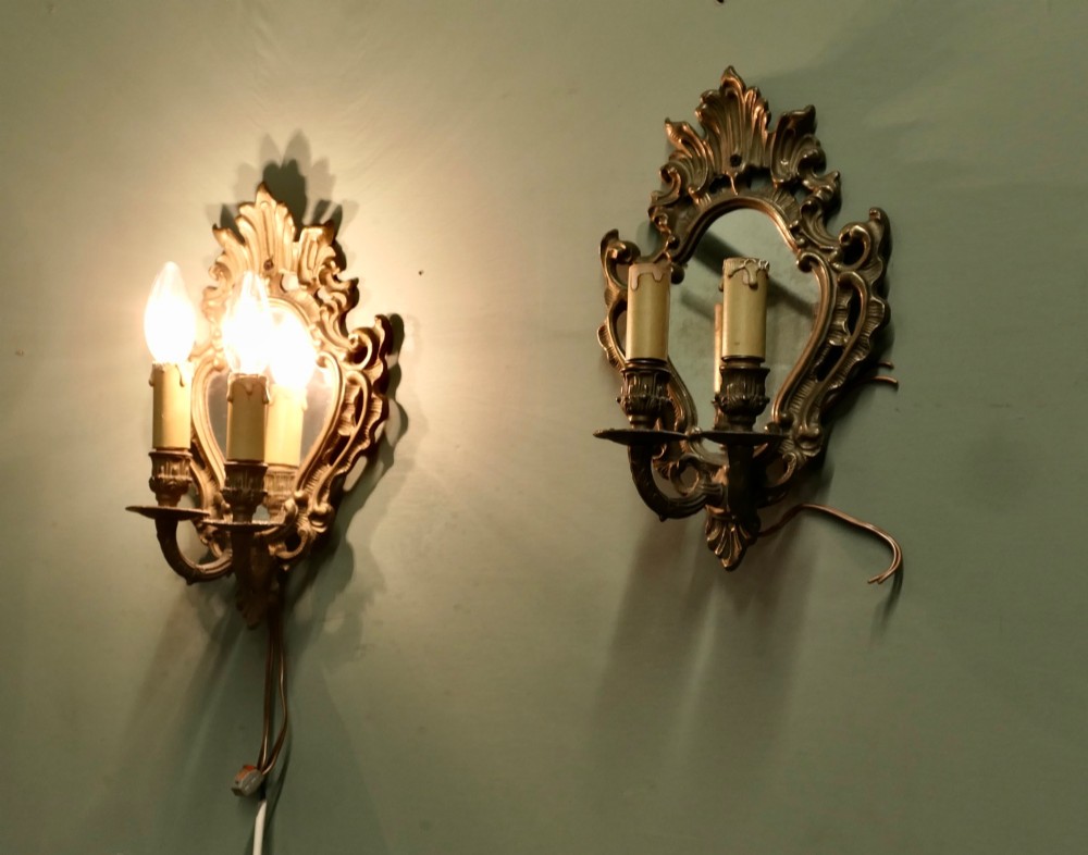 A pair of ornate gilt brass Rococo wall sconces featuring oval central mirrors and twin candle-style light fittings. View II