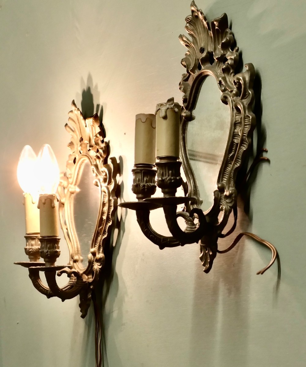 A pair of ornate gilt brass Rococo wall sconces featuring oval central mirrors and twin candle-style light fittings. View III