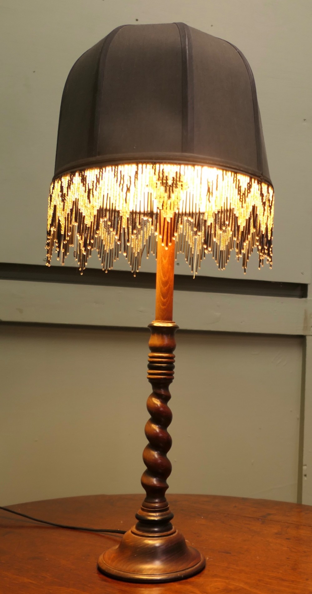 A wooden table lamp featuring a turned barley twist stem and a dark dome shade adorned with glass bead fringe.