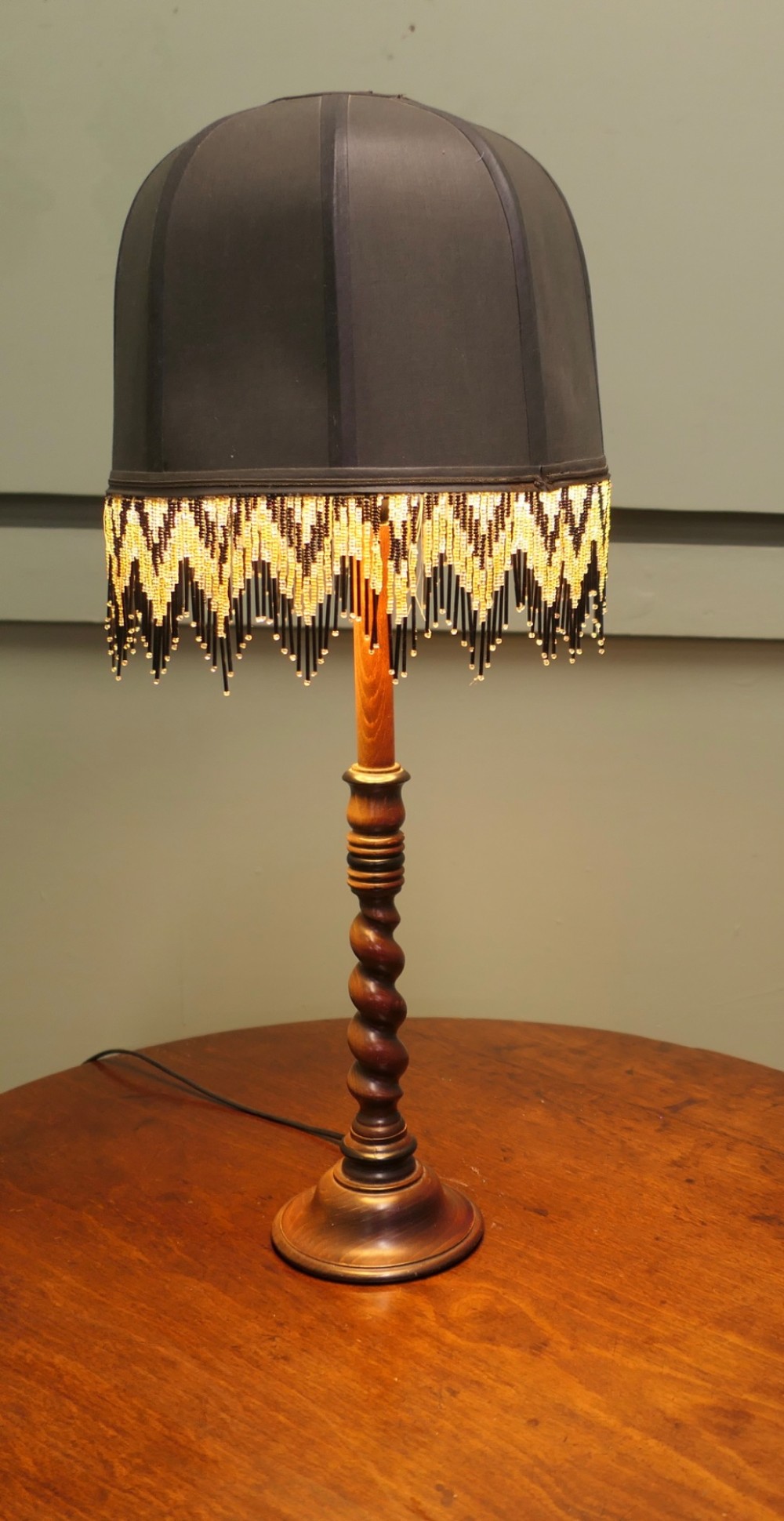 A wooden table lamp featuring a turned barley twist stem and a dark dome shade adorned with glass bead fringe. View II