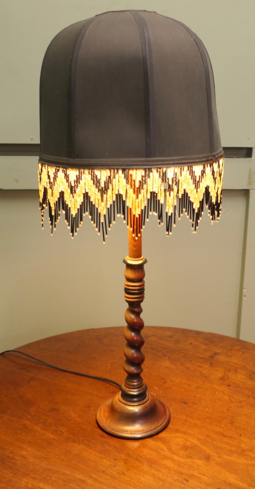 A wooden table lamp featuring a turned barley twist stem and a dark dome shade adorned with glass bead fringe. View V