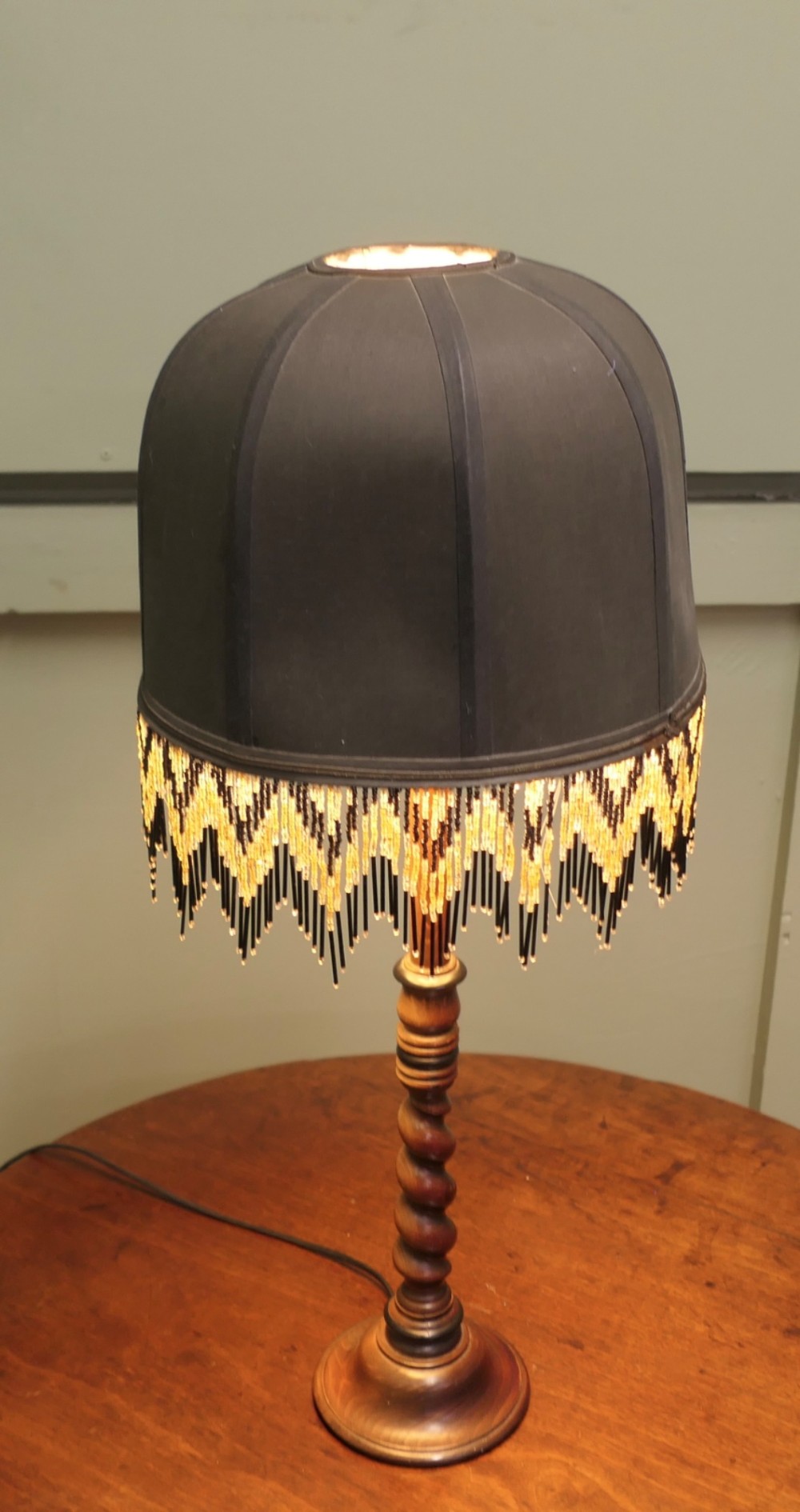 A wooden table lamp featuring a turned barley twist stem and a dark dome shade adorned with glass bead fringe. View VI