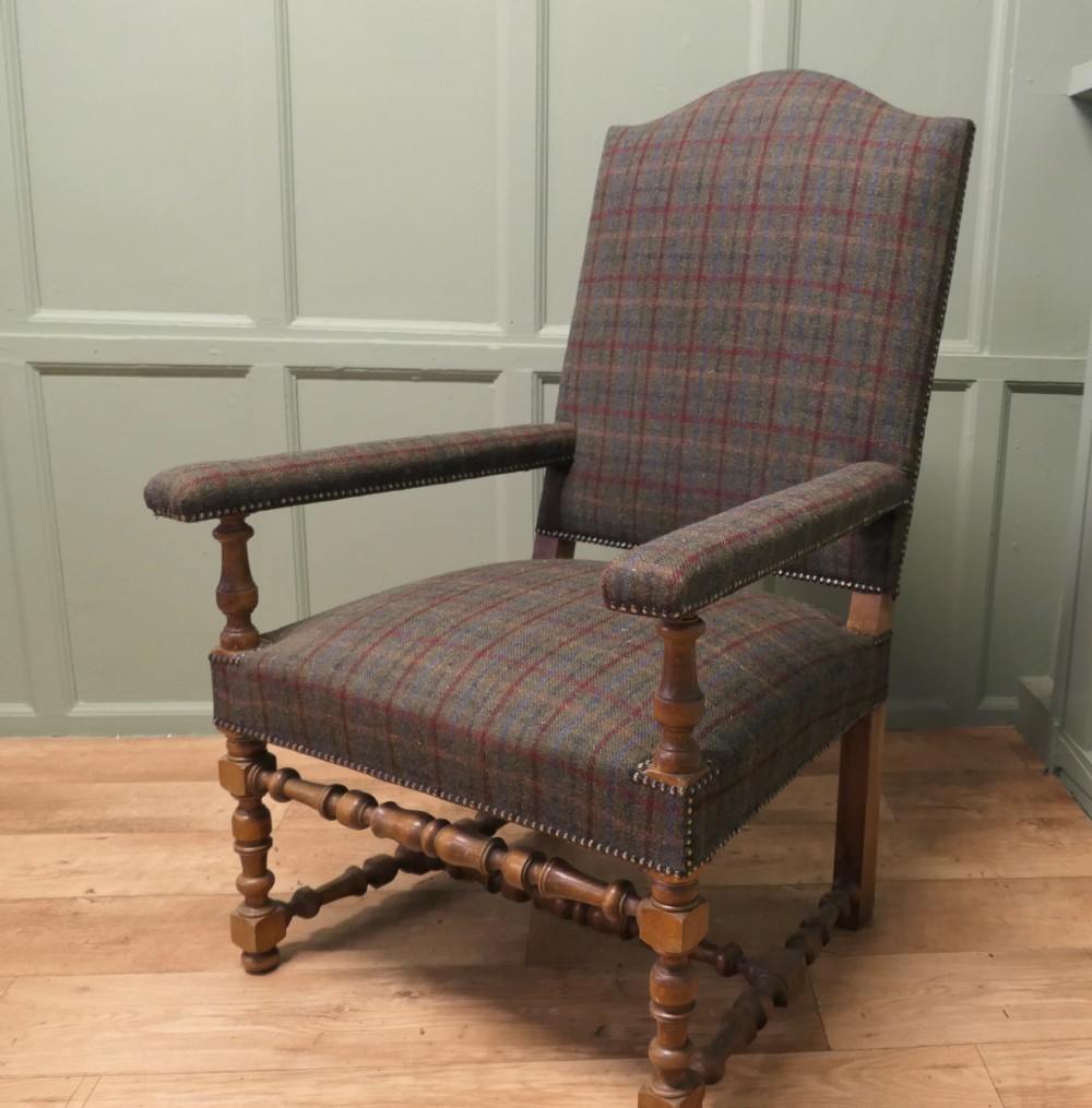 An upholstered high-back armchair with tweed plaid fabric, brass studding, and turned oak legs with stretchers.