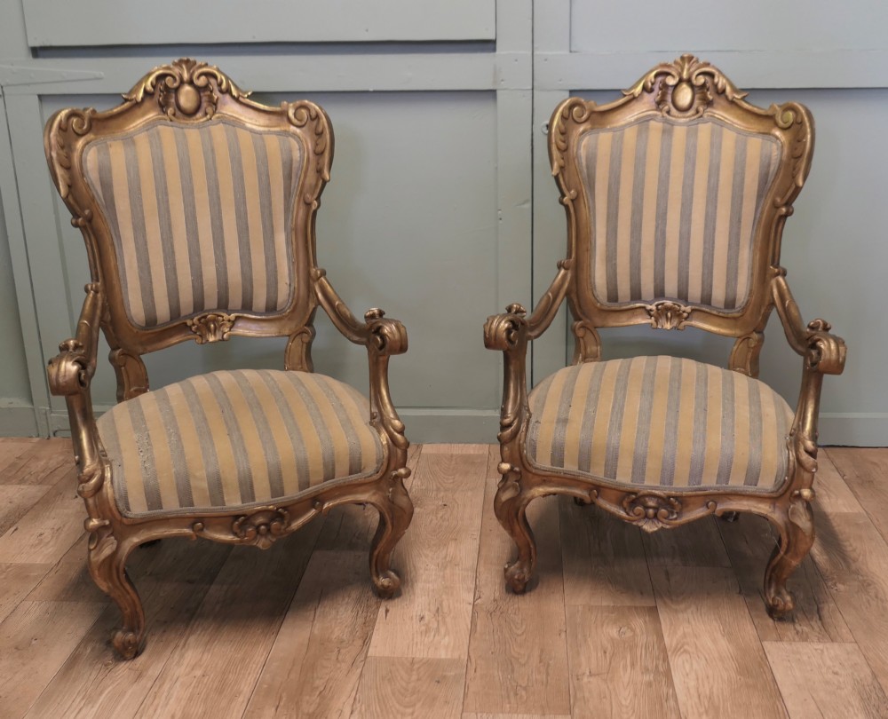 A pair of ornate Italian Rococo style armchairs with carved giltwood frames and grey and gold striped upholstery.