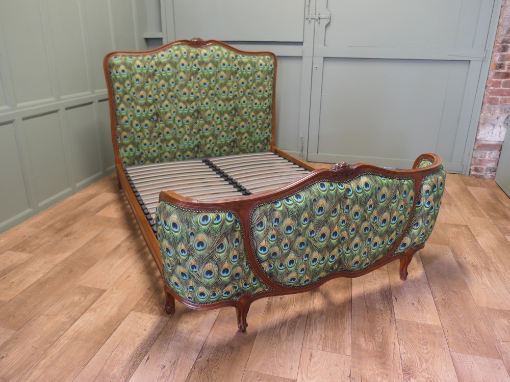 A French Louis XV style double bed frame featuring carved wooden borders, a padded headboard, and a curved corbeille footboard upholstered in green peacock feather patterned fabric with studding. View II